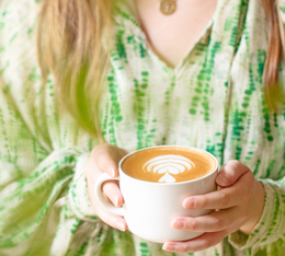 latte art bio dans une tasse blanche tenue par une femme en chemise verte tiedye cafe green lion coffee ethique et artisanal